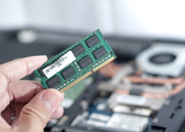 Arka planda açık dizüstü bilgisayarı olan bir teknisyenin yedek bellek tutarken ki görüntüsü bulanık. Donanım kurulumu veya güncellemesinden önceki anı yakalar.