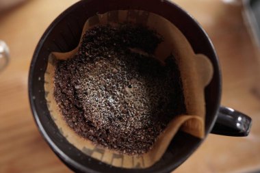 Detaylı, yukarıdan çekilmiş bir çekim, ıslak, köpüren kahve öğütücülerini, bulanık ahşap bir yüzeyde koyu kahve damlatıcısının içine yerleştirilmiş kahve telvelerini ve lezzetli bir günlük kahve fincanını gösteren büyüleyici süreci yakalar..