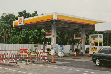 Jakarta - Endonezya, 02 / 03 / 2026: Çok sayıda yakıt pompası, siyah bir sedan ve geçici kırmızı ve beyaz güvenlik bariyerlerinin yer aldığı bir açık hava fotoğrafı. Bereketli tropikal ağaçlar bulutlu bir gökyüzünün altında arka planda..