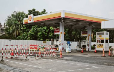 Jakarta - Endonezya, 02 / 03 / 2026: Terk edilmiş bir Shell benzin istasyonunun dış görünüşü, belirgin sarı ve kırmızı bir gölgelik altında birden fazla V-Power yakıt pompası ortaya çıkardı. Ön planda kırmızı ve beyaz güvenlik bariyerleri kuruldu.,