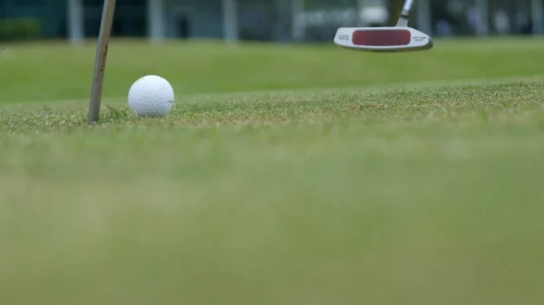 Golf player putting ball into hole, only feet and iron to be seen