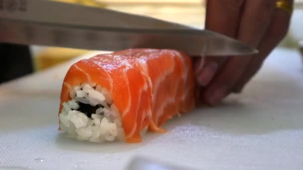 Memasak sushi gulung di studio. memotong ke bagian-bagian, gulungan bulat beras, salmon, herbal segar — Stok Video