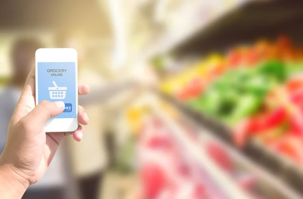 Ekranda online alışveriş bakkal ile akıllı telefon tutan el 