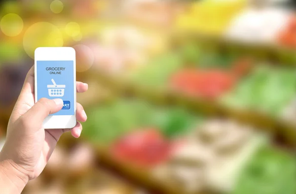 Ekranda online alışveriş bakkal ile akıllı telefon tutan el 