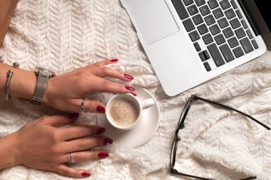 Woman's hands, holding cup of coffee using laptop computer and glasses
