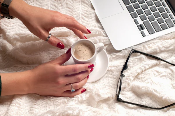 Женские руки, держа чашку кофе с помощью ноутбука и очков — стоковое фото