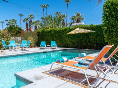 Palm Springs, Kaliforniya 'da gündüz vakti renkli şezlongları olan yüzme havuzunun arka bahçesi.