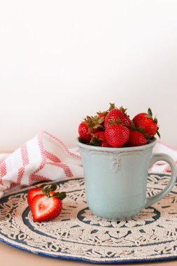 Eski paslı mug içinde taze sulu çilek. Rustik ahşap arka plan desenli tığ işi peçete ile.