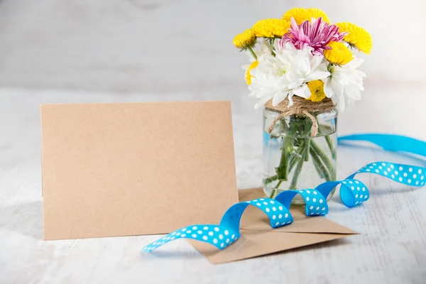 Bouquet de fleurs dans un vase en pot avec note de carte, enveloppe et ruban bleu sur un fond rustique en bois blanc — Photo