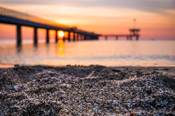 Zand op het strand. Onscherpe achtergrond van brug en zonsopgang. — Stockfoto