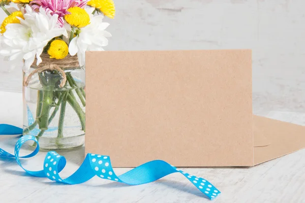 Bouquet de fleurs dans un vase en pot avec note de carte, enveloppe et ruban bleu sur un fond rustique en bois blanc — Photo