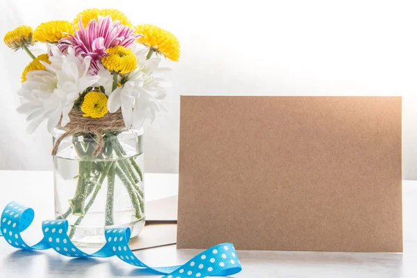 Bouquet de fleurs dans un vase en pot avec note de carte, enveloppe et ruban bleu sur un fond rustique en bois blanc — Photo