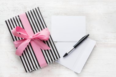 Boş tebrik kartı. Sarılmış hediye, zarf ve kalem Beyaz ahşap zemin üzerinde.