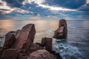 Bir kayalık plaj üzerinde gündoğumu. Denizde yansıtan renkli bulutlar