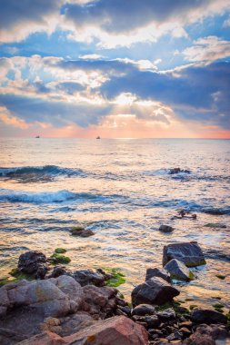 Bir kayalık plaj üzerinde gündoğumu. Denizde yansıtan renkli bulutlar