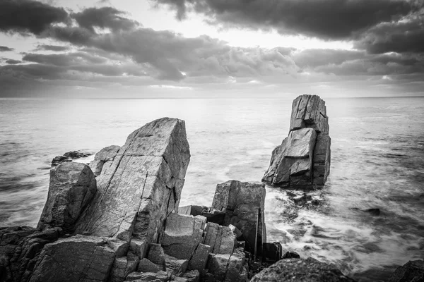 Bir kayalık plaj üzerinde gündoğumu. Denizde yansıtan renkli bulutlar.
