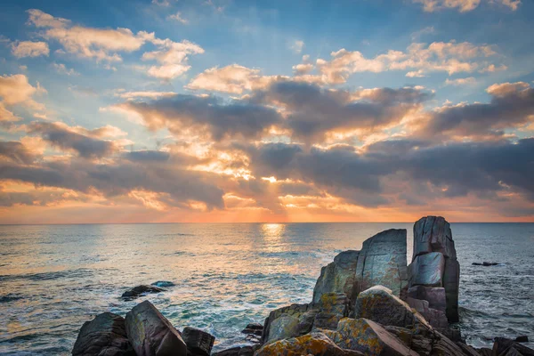 Bir kayalık plaj üzerinde gündoğumu. Denizde yansıtan renkli bulutlar