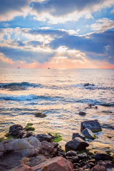 Bir kayalık plaj üzerinde gündoğumu. Denizde yansıtan renkli bulutlar