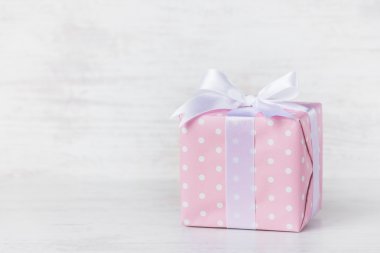 Hediye kutusu pembe noktalı kağıt sarılı ve saten yay bir beyaz tahta arka plan üzerinde bağlı. 