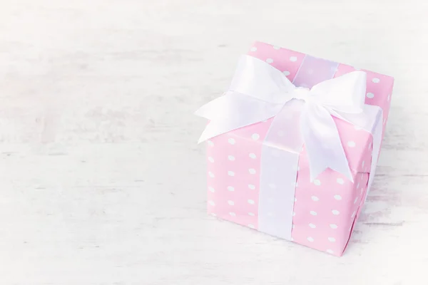 Ajándék doboz papírba csomagolva rózsaszín pontozott, és kötött szatén íj, mint egy fehér fa háttér. — Stock Fotó