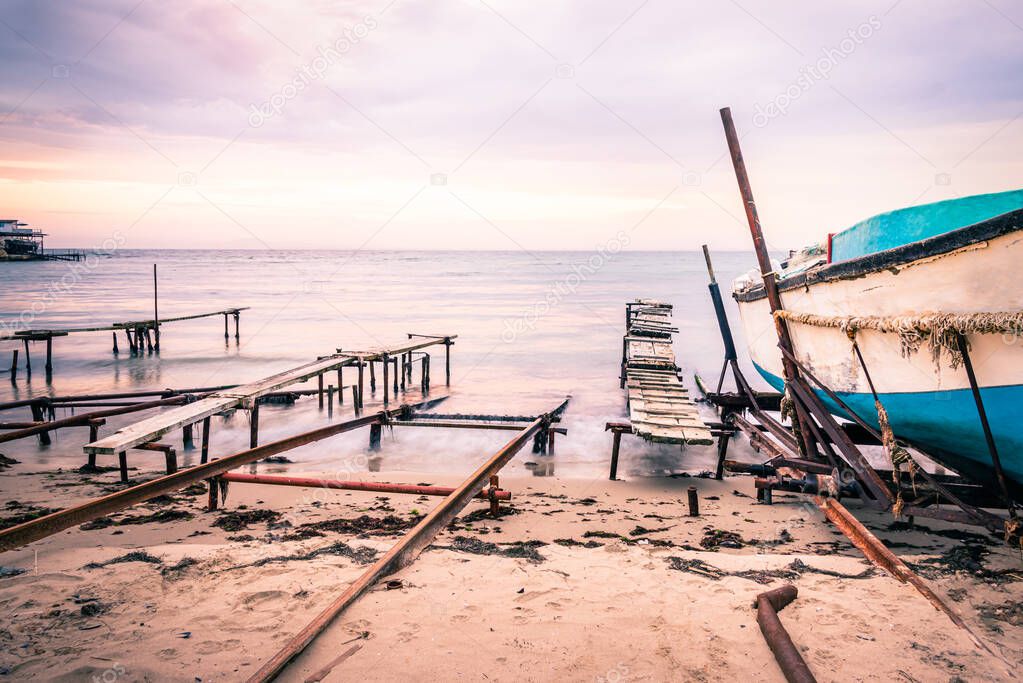 Colorful sunset over the sea shore. Old rusty boat berths. Long exposure smooth water waves effect.