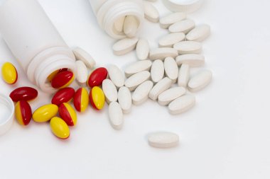 Close up of soft red and yellow gelatin capsules and white tablets scattered with the bottles on a white background