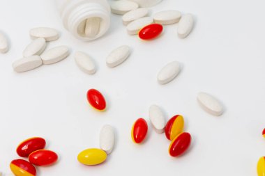 Close up of soft red and yellow gelatin capsules and white tablets scattered with the bottles on a white background