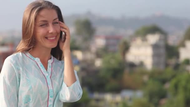 Felice bella donna che parla telefono, utilizzando smartphone, sorridente, godendo la vita. vale la pena per il suo petto sul tetto grande città all'aria aperta. Kathmandu, Nepal — Video Stock