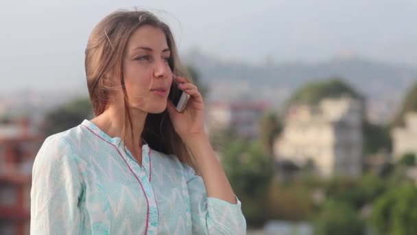 Mulher jovem bonita profissional tem uma conversa telefônica no telhado do escritório Varanda na cidade durante o dia. Ela fica de pé até a cintura dele, sorrindo e desenvolvendo o cabelo em um vento. Katmandu, Nepal — Vídeo de Stock