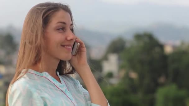 Belle jeune femme professionnelle a une conversation téléphonique sur le toit du balcon de bureau dans la ville pendant la journée. Elle se lève jusqu'à sa taille, souriant et cheveux se développant sur un vent. Katmandou, Népal — Video