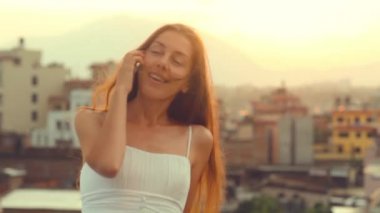 Cep telefonu genç kadın Smartphone Sun City günbatımı üzerinde söz. Rüzgar çırpınan cep telefonu saçının konuşmayı gülüyor gülümseyen genç profesyonel. Yaz, Katmandu, Nepal.