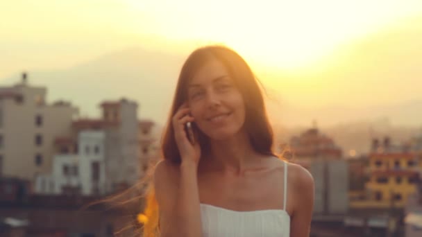 Cep telefonu genç kadın Smartphone Sun City günbatımı üzerinde söz. Rüzgar çırpınan cep telefonu saçının konuşmayı gülüyor gülümseyen genç profesyonel. Yaz, Katmandu, Nepal. — Stok video