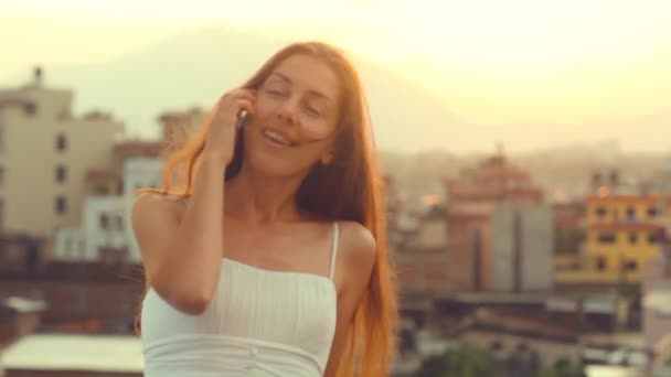 Cellulare Giovane donna che parla sul tramonto Smartphone Sun City. Giovane professionista sorridente che ride avendo conversazione sul telefono cellulare capelli fluttering Wind. Summer, Kathmandu, Nepal . — Video Stock