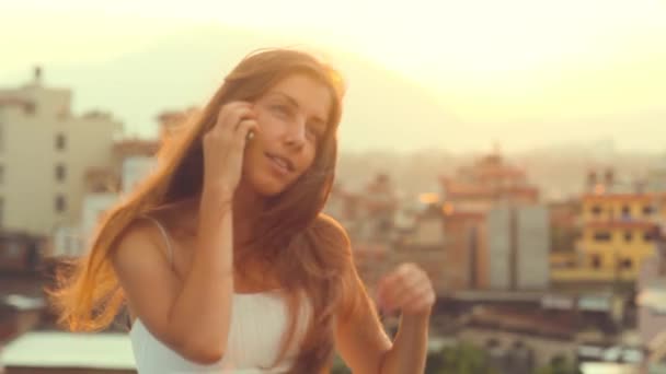 Teléfono celular Mujer joven hablando en el teléfono inteligente Sun City Sunset. Joven profesional sonriente riendo tener conversación en el teléfono móvil pelo aleteo viento. Summer, Katmandú, Nepal . — Vídeo de stock