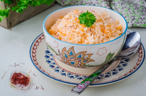 Rice pilaf with saffron in ornament bowl on wooden background. Selective focus — Stockfoto