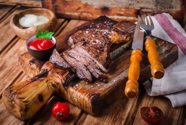 Ahşap arka plan üzerinde kesme tahtası üzerinde baharat ve ketçap ile Dilimlenmiş orta nadir ızgara Beef biftek