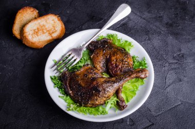 Kekik ile Confit ördek bacaklar koyu arka plan salata ile beyaz tabakta servis edilir. Seçici odaklama