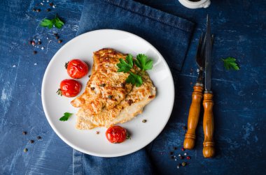 Koyu mavi arka planda beyaz kapta domates, maydanoz ve baharat ile kavrulmuş hindi biftek. Seçici odak. Tonlu görüntü