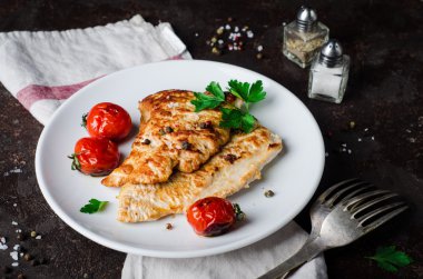 Koyu kayrak arka planda beyaz kapta domates, maydanoz ve baharat ile kavrulmuş hindi biftek. Seçici odak. Tonlu görüntü