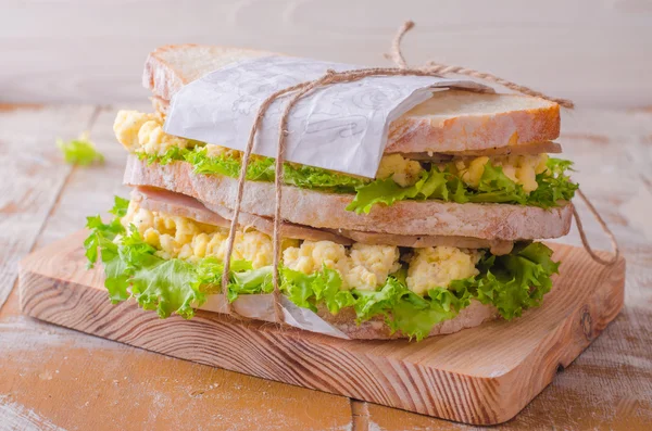 Sandwich aux œufs brouillés, feuilles de salade et jambon sur une bassinière en bois. Concentration sélective — Photo