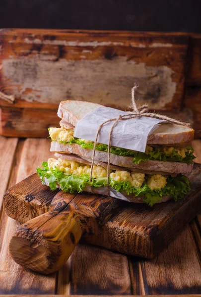 Sandwich aux œufs brouillés, feuilles de salade et jambon sur une bassinière en bois. Concentration sélective — Photo