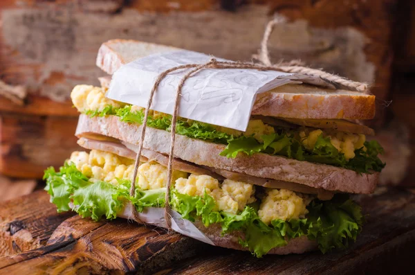Sandwich aux œufs brouillés, feuilles de salade et jambon sur une bassinière en bois. Concentration sélective — Photo