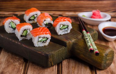 Suşi rulo somon ve salatalık ile soya sause ve zencefil şeklinde ahşap tahta üzerinde ahşap arka plan gül yılları arasında görev yapmıştır. Seçici odak