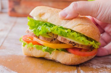Sandwich with roasted chicken, leaves salad and tomatoes on wooden baskgraund. Selective focus