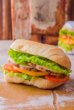 Sandwich with roasted chicken, leaves salad and tomatoes on wooden baskgraund. Selective focus