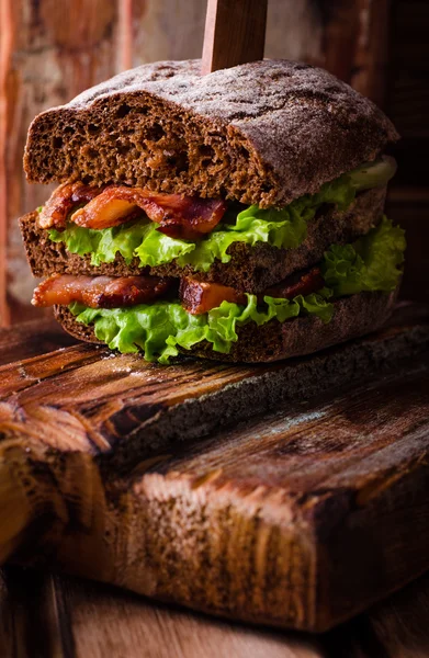 Σάντουιτς burger με μαρούλι, ψητό μπέικον σε σκούρο ξύλο σανίδα κοπής. Επιλεκτική εστίαση — Φωτογραφία Αρχείου
