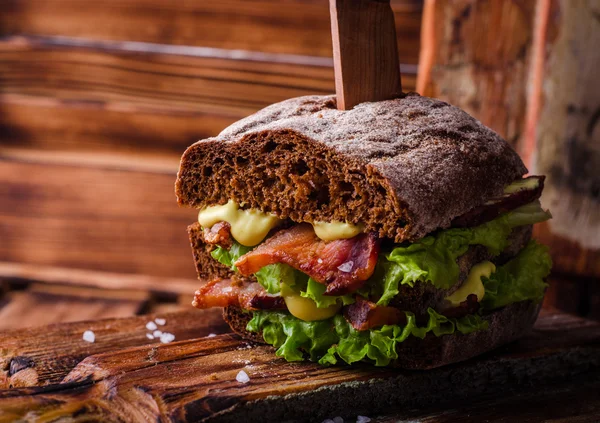 Burger-Sandwich mit Salat, gebratenem Speck auf dunklem Holzschneidebrett. Selektiver Fokus — Stockfoto