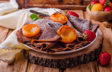 Ahşap arka plan üzerinde çilek ve ızgara kayısı ile süslenmiş çikolata krep yığını. Seçici odaklama.