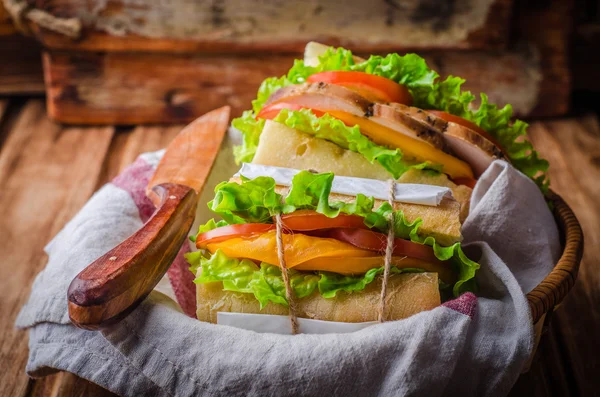 Homemade sandwich with fresh tomatoes and chicken breast in basket on wooden background. Selective focus. Picnic concept — Stock Photo, Image