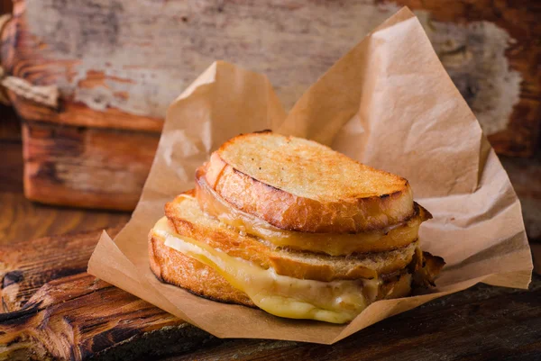 Сэндвич с сыром на бумаге на деревянной доске. Селективный фокус. — стоковое фото